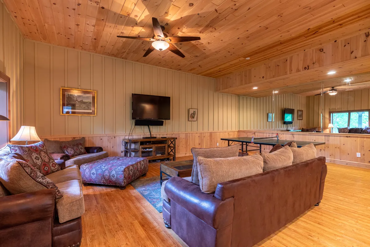 A cozy living room with a spacious sectional facing a large television, with a ping pong table set off to the side. Warm lighting and decorative wall art contribute to the inviting family atmosphere, ideal for both watching movies and engaging in friendly competition.