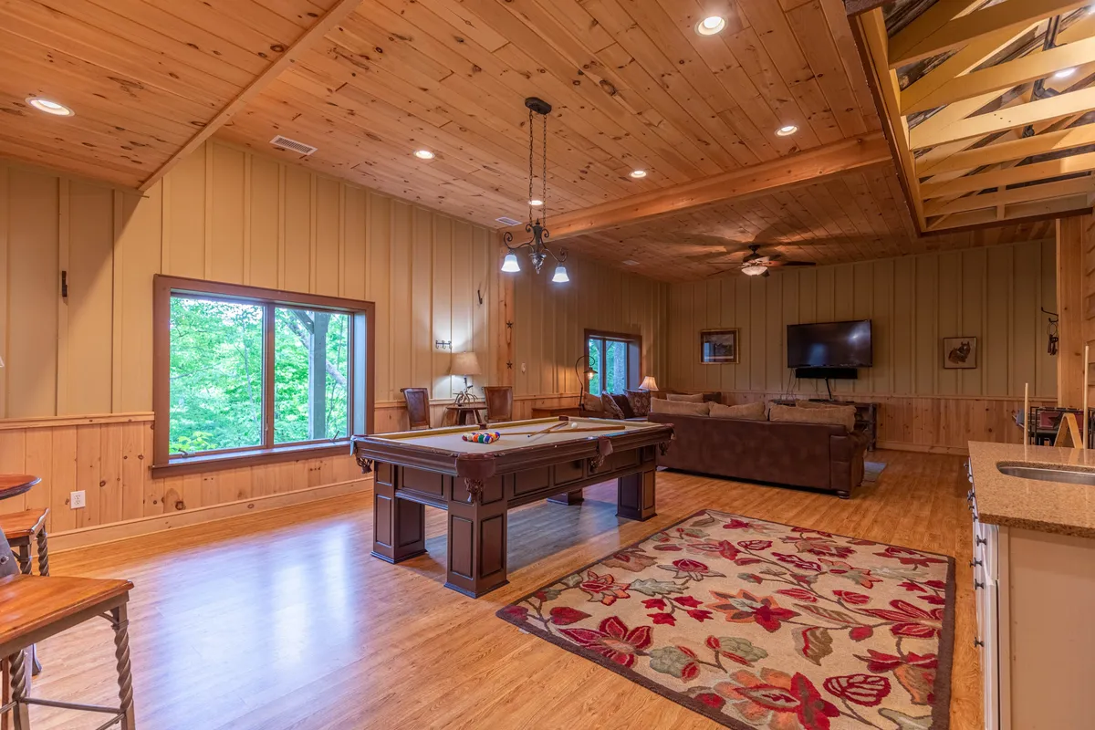 A spacious, sunlit game room with a pool table, comfortable sofa, and large windows revealing the outdoors. The room is designed for friendly competitions, social gatherings, and relaxation, capturing the essence of in-home entertainment for all ages.