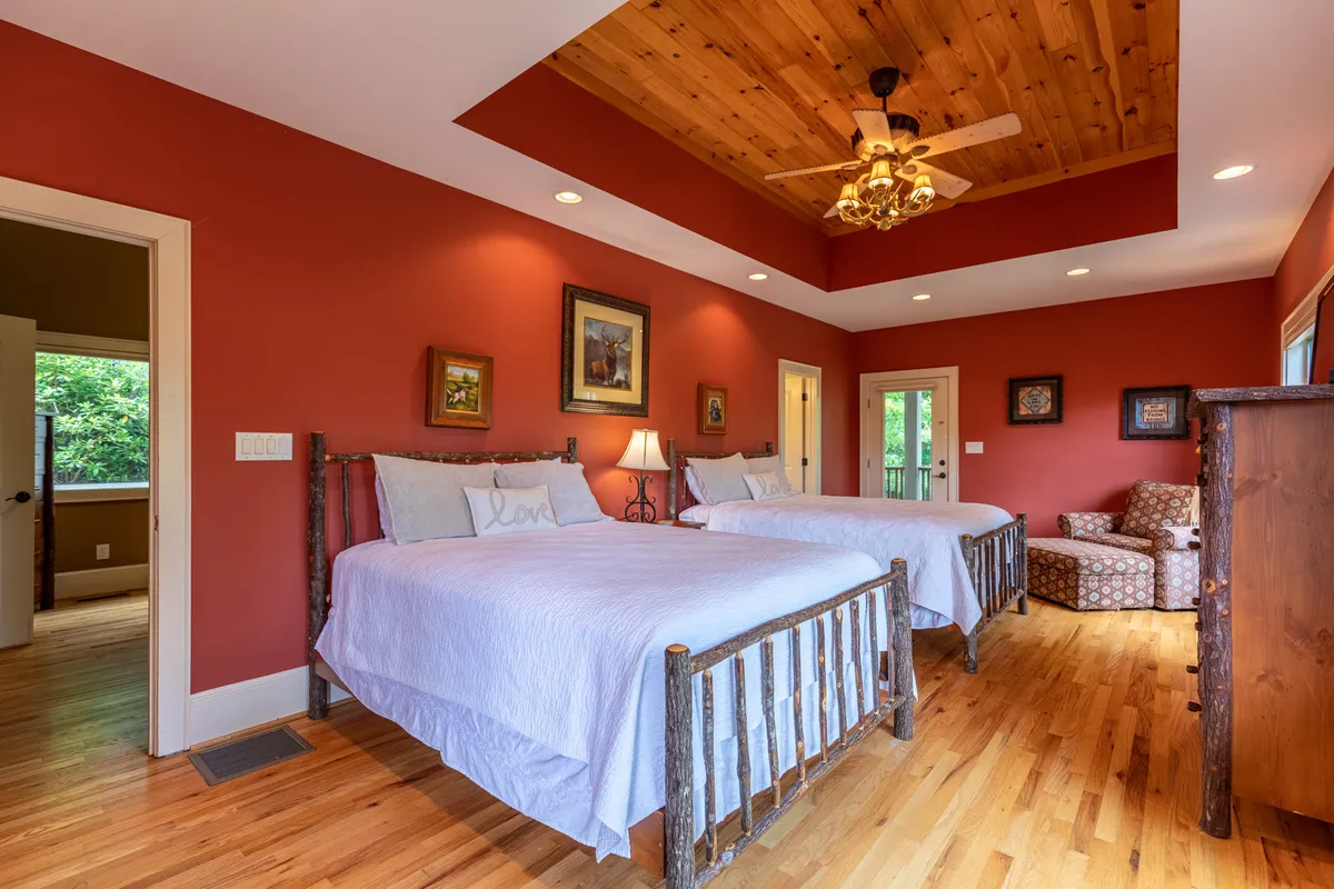 A spacious bedroom with two large beds, a wooden ceiling fan, a cozy armchair, and framed artwork on the walls. The layout is perfect for families or groups wanting to share a comfortable space.