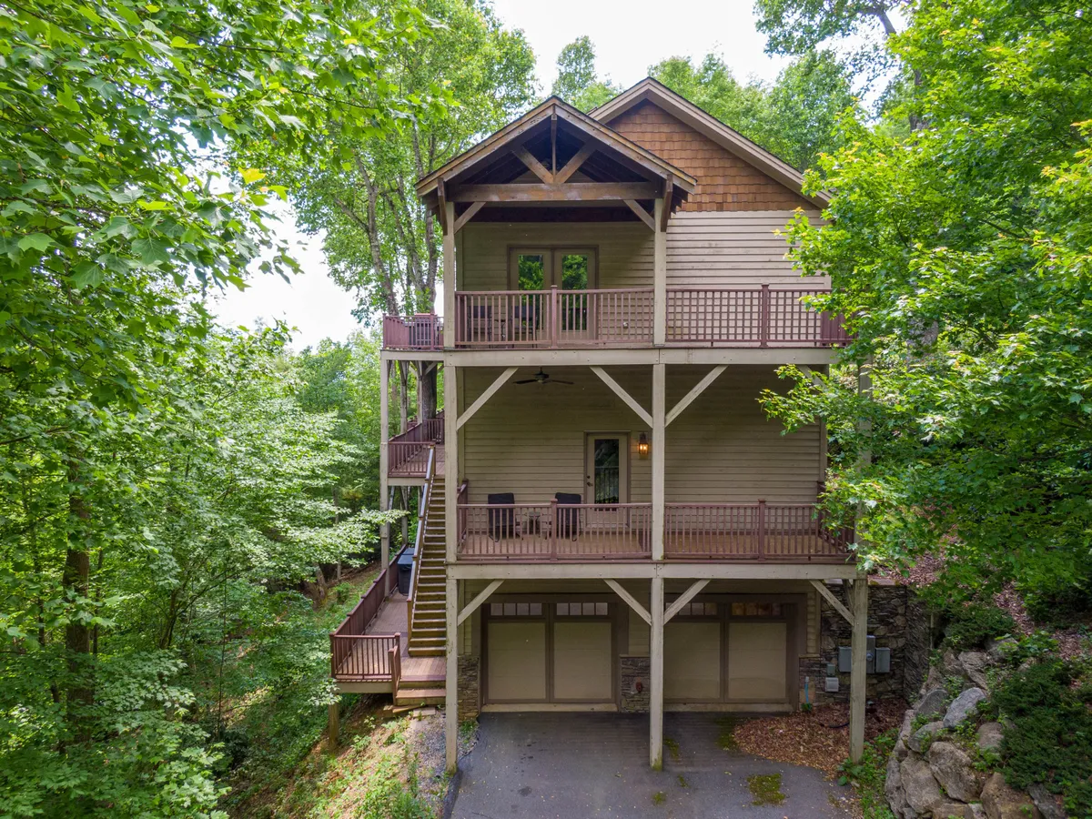A striking exterior view of a large three-story mountain home, featuring wooden balconies and surrounded by lush greenery. The setting conveys an inviting and spacious environment, ideal for accommodating large groups or families. The balconies hint at outdoor gathering spots and the natural landscape frames the house, highlighting its connection to the High Country outdoors.