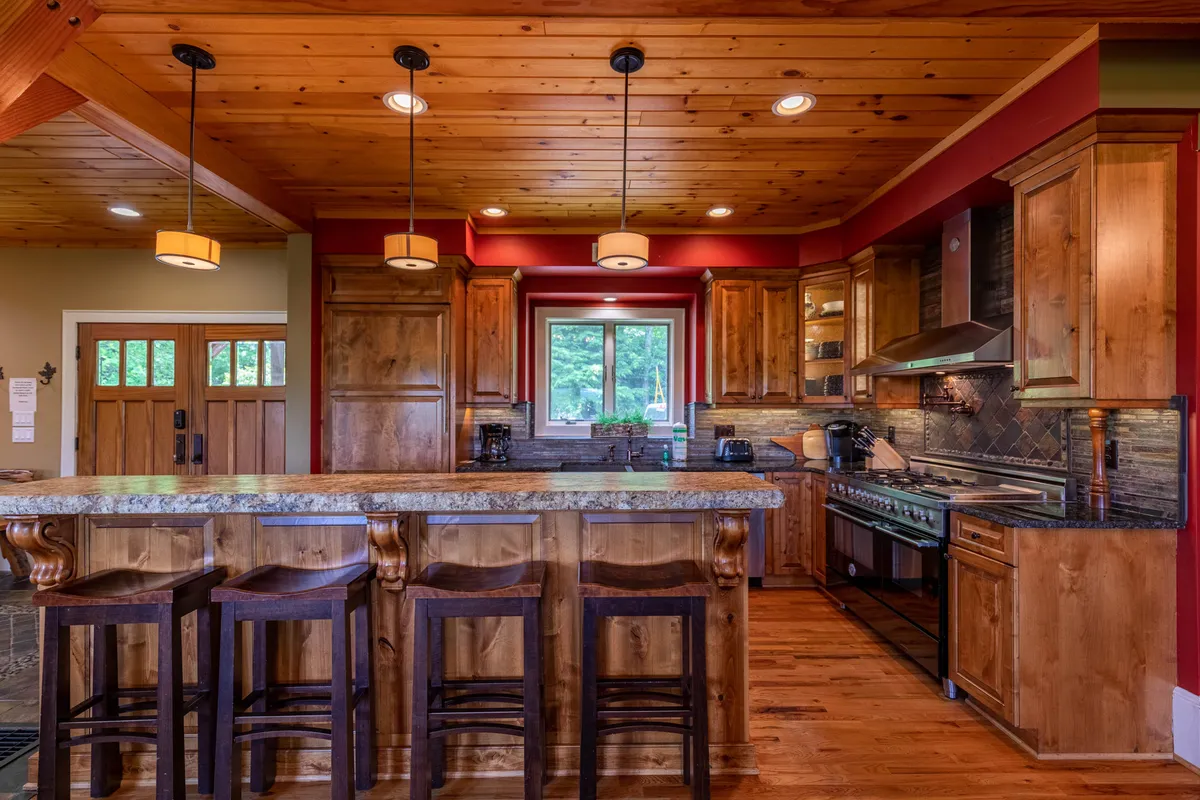 A gourmet kitchen featuring a prominent kitchen island with a granite countertop, custom wooden cabinetry, and professional-grade appliances. Sunlight streams through a window, highlighting the welcoming, open layout ideal for both everyday use and entertaining.