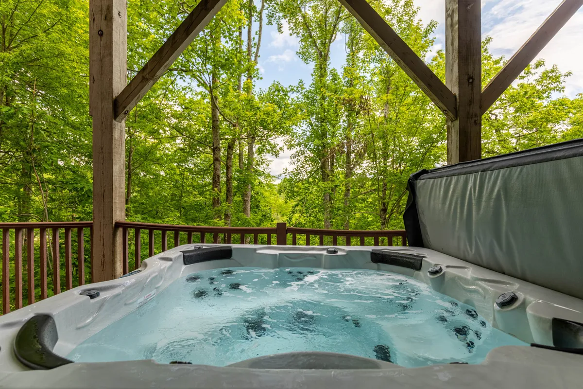 This exterior image captures a hot tub nestled on a wooden deck, surrounded by lush greenery. The design is inviting, with the structure blending seamlessly into the natural mountain setting, offering both privacy and scenic views.