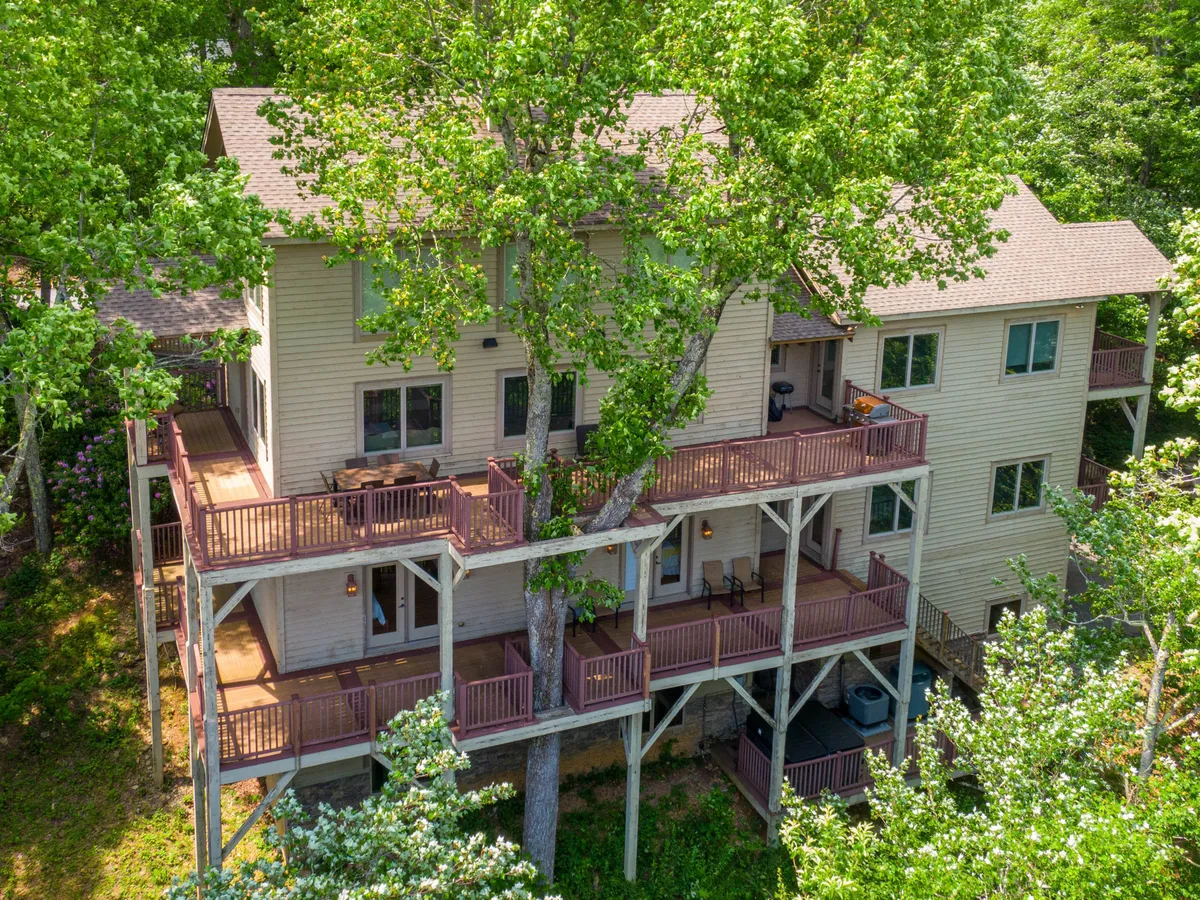 A spacious multi-level deck surrounded by tall trees, with multiple outdoor seating areas. The deck offers a sense of privacy and ample space for group gatherings, outdoor meals, and socializing, while the lush greenery creates a tranquil atmosphere.