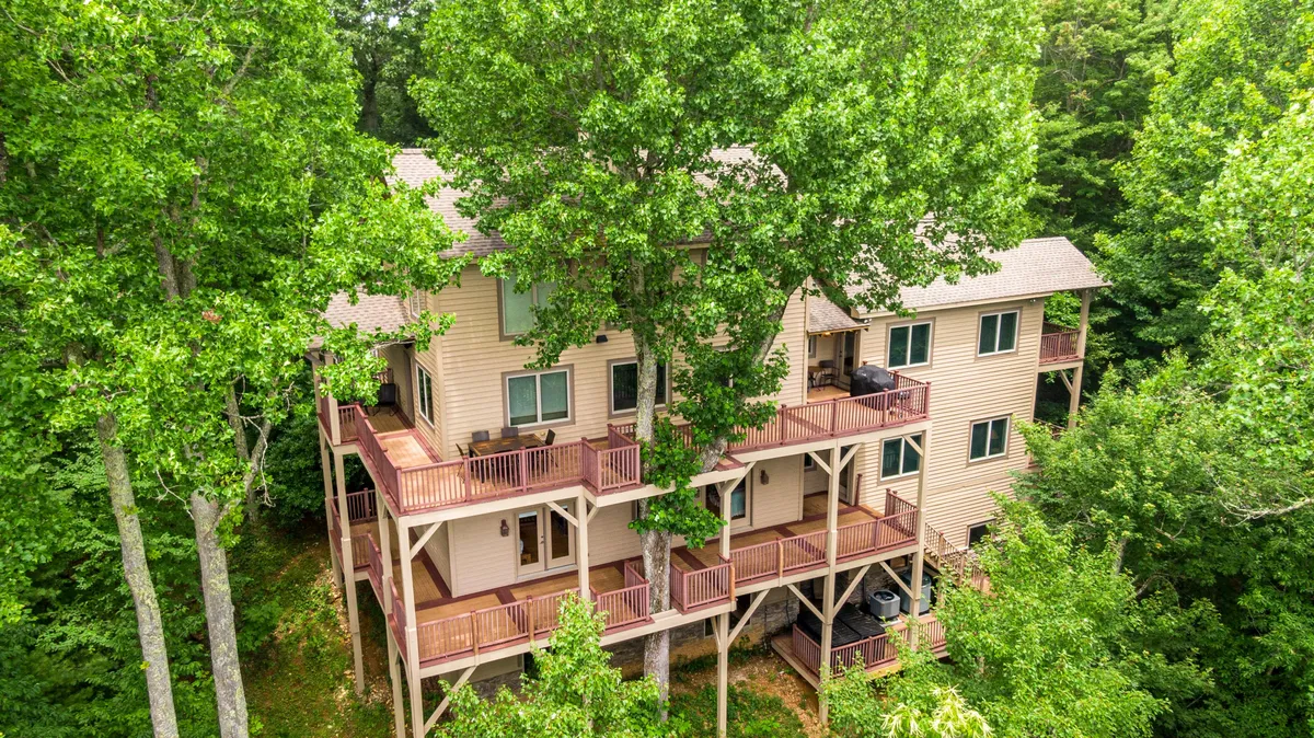A wide exterior view of the home shows multi-level decks surrounded by tall trees and natural landscaping. The decks offer ample outdoor living space, perfect for socializing, relaxing, and enjoying the mountain air.