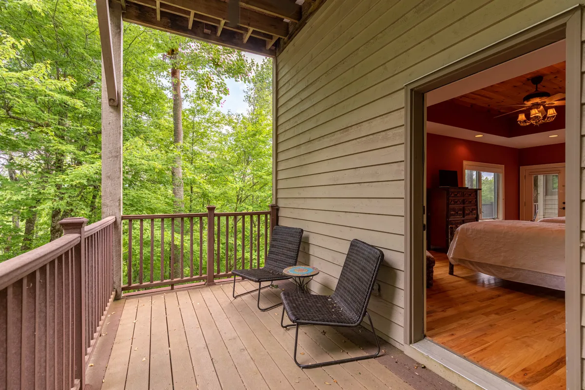 An exterior shot of a private balcony with comfortable chairs and a small table overlooks lush greenery. The open doorway into a bedroom hints at easy transitions between indoor comfort and outdoor serenity.