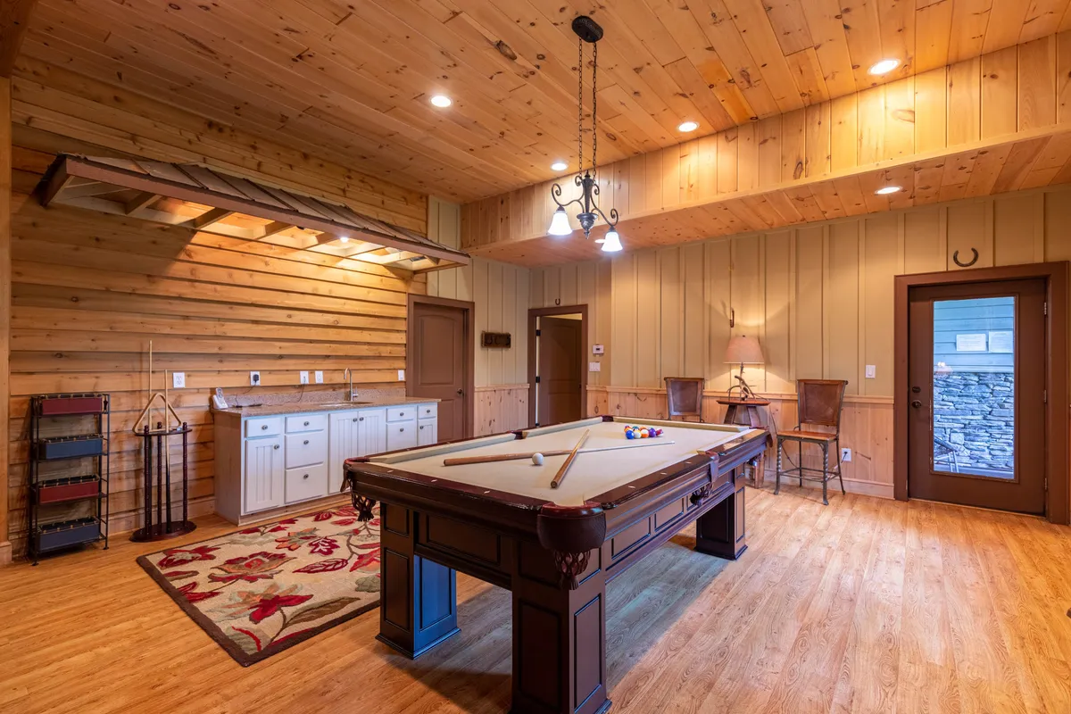 A cozy game room with a classic pool table, warm wooden walls, a striking chandelier, and an inviting area rug—ideal for gathering after a day of adventure.