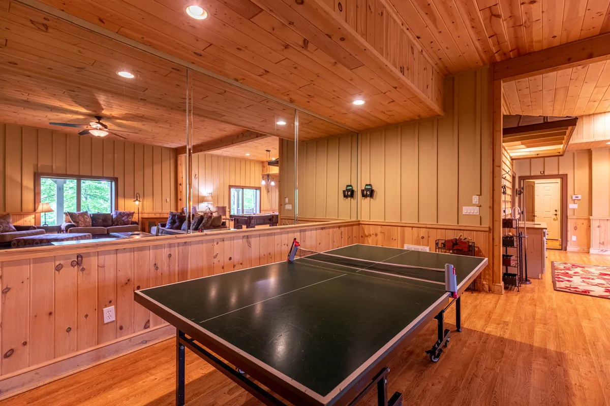 A playful game room featuring a ping pong table, comfortable seating, and wood-paneled walls. The mirrored wall adds depth, and the cozy seating area invites guests to relax between games. The atmosphere is casual and energetic, perfect for friendly competitions and group fun.